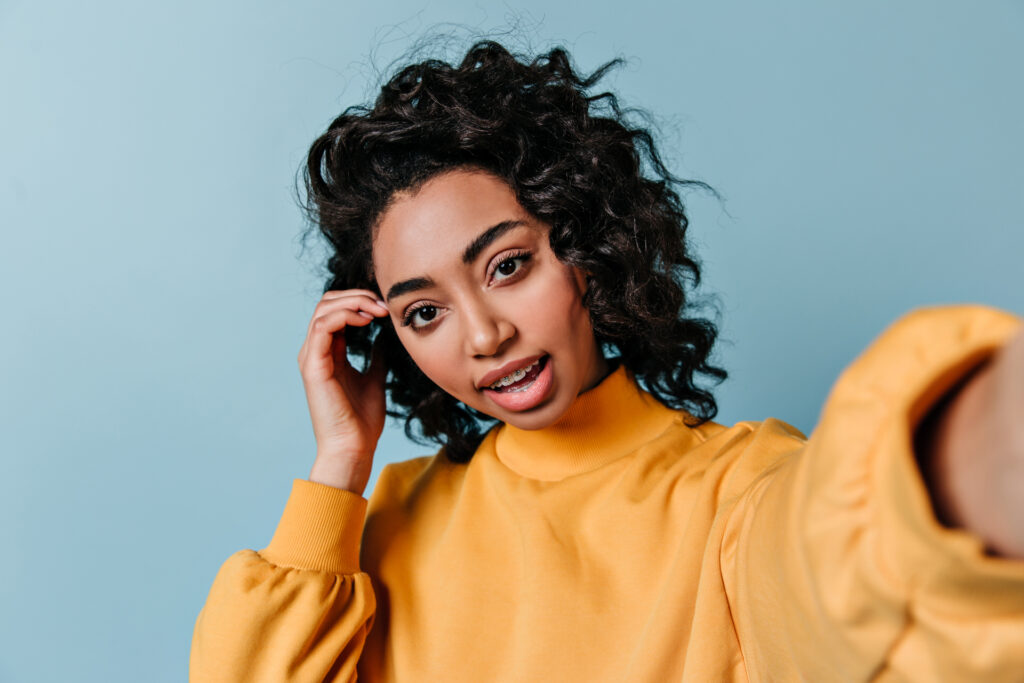 Interested brunette girl taking selfie. Front view of beautiful mixed race woman in yellow sweatshirt.