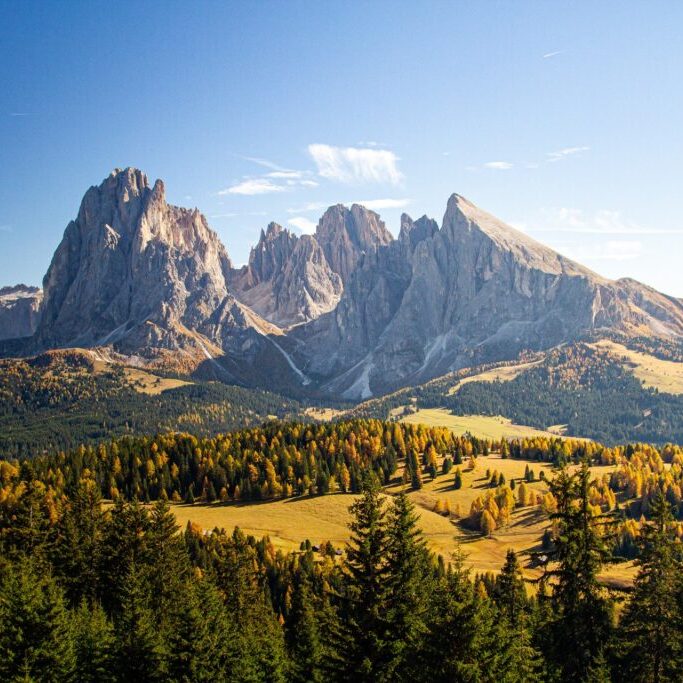 Beautiful shot of grassy hills covered in trees near mountains in Dolomites Italy a beautiful shot of grassy hills covered in trees near mountains in Dolomites Italy