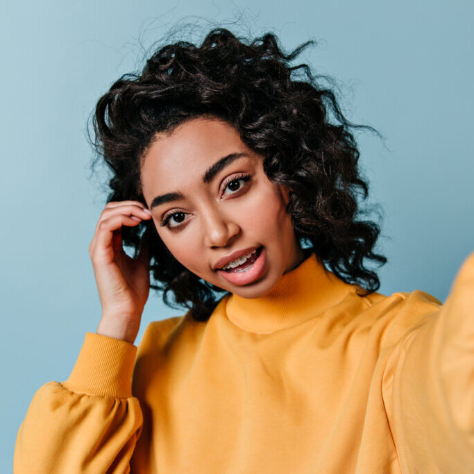 Interested brunette girl taking selfie. Front view of beautiful mixed race woman in yellow sweatshi Interested brunette girl taking selfie. Front view of beautiful mixed race woman in yellow sweatshirt.